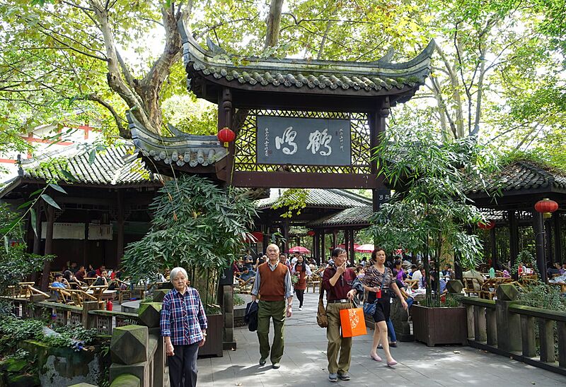 成都人民公园鹤鸣茶馆入口,鹤鸣匾额下的竹椅茶席与来往茶客